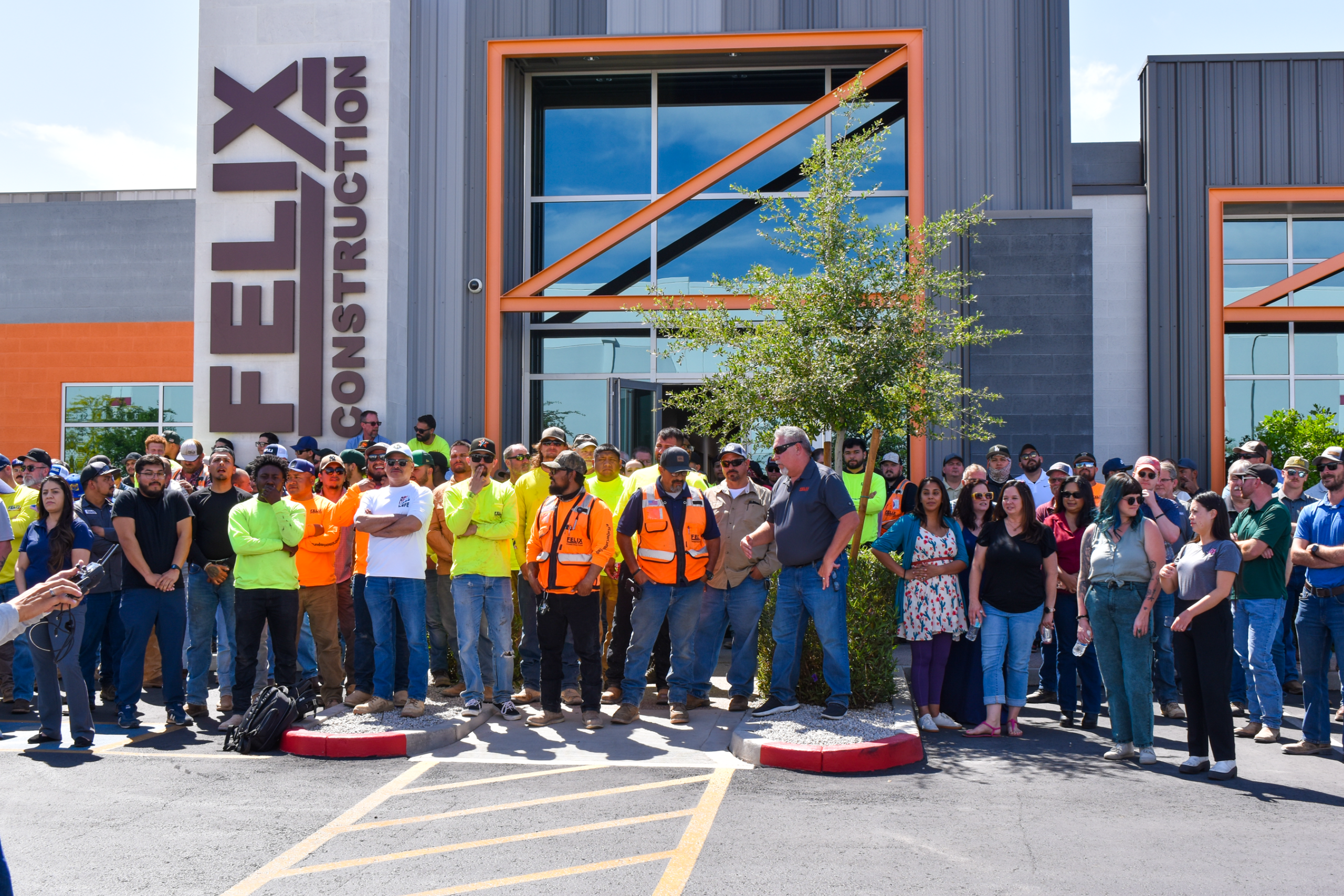 A large group of people, some in construction attire and safety vests, pose for a photo in front of a building labeled "Felix Construction.